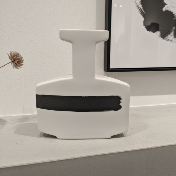 Modern minimalist white ceramic vase with black brush stroke design on a concrete shelf