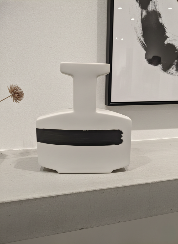 Modern minimalist white ceramic vase with black brush stroke design on a concrete shelf
