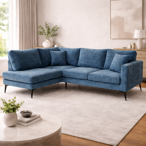 Blue velvet L-shaped sectional sofa with plush scatter cushions and slim black metal tapered legs, styled in a warm neutral living room with ceramic vases and soft natural light.