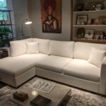 White boucle L-shaped sectional sofa with a left-facing chaise lounge and plush scatter cushions, styled in an eclectic living space with original artwork, open shelving, and a marble coffee table.