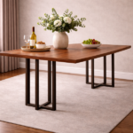 Large rectangular dining table with metal legs in dark bronze U-bracket design and a warm walnut wood top, styled with a floral centrepiece, wine bottle, and fruit bowl in a neutral dining room.