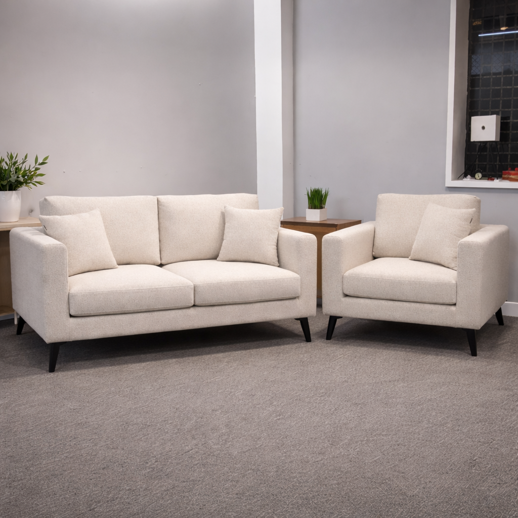 cream sofa Cream sofa and armchair set with black tapered legs, both pieces upholstered in a soft oatmeal fabric with scatter cushions, styled together in a clean showroom setting with a side table and greenery.