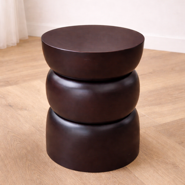 Dark sculptural side table with three stacked organic rings in a deep espresso matte finish, placed on a light oak herringbone floor against a white wall.