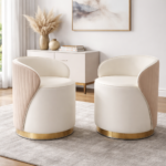 A pair of cream velvet vanity stools with gold base rings, featuring channel-tufted blush pink outer backs and curved barrel silhouettes, styled in a glam neutral bedroom with pampas grass and abstract art.