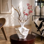 White geometric ceramic vase with gold accents and red branches on a round wooden side table.