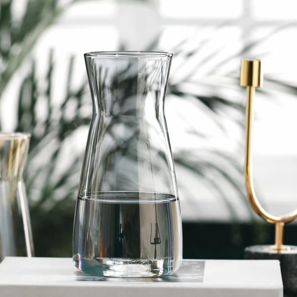Modern transparent glass vase and water carafe on a white table with minimalist luxury interior background