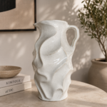 White ceramic pitcher vase with leaf texture on a modern table in a neutral living room.