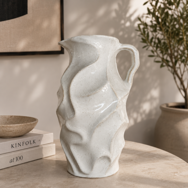 White ceramic pitcher vase with leaf texture on a modern table in a neutral living room.