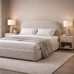 Beige upholstered bed with a curved headboard, textured fabric finish, white bedding, and modern bedside tables in a calm bedroom